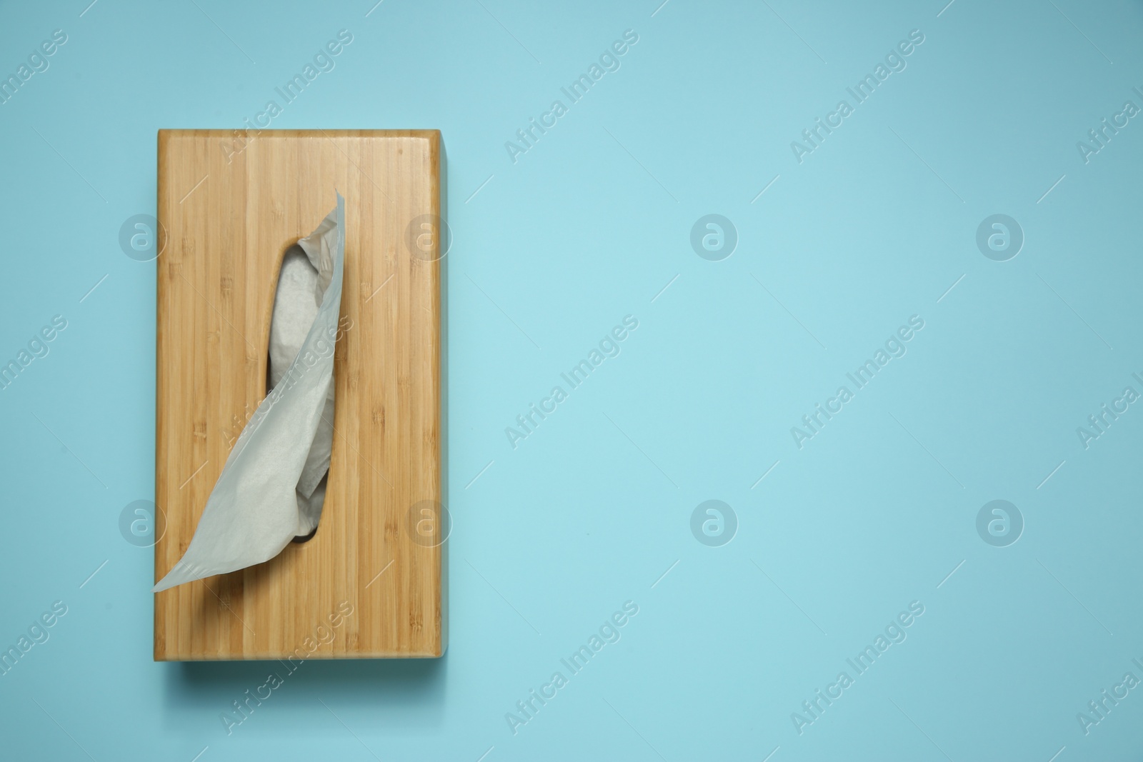 Photo of Wooden holder with paper tissues on light blue background, top view. Space for text