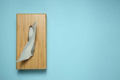 Wooden holder with paper tissues on light blue background, top view. Space for text