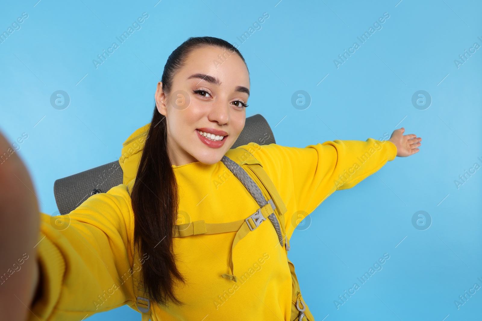 Photo of Smiling young woman with backpack taking selfie on light blue background. Active tourism