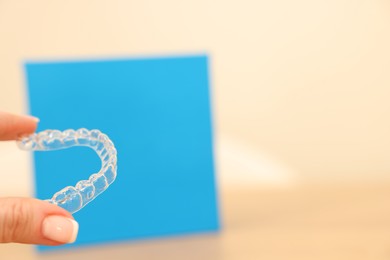 Photo of Woman with transparent dental aligner on blurred background, closeup. Space for text