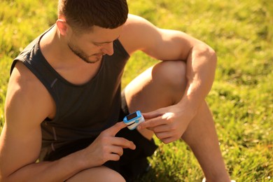 Attractive man checking pulse with blood pressure monitor on finger after training outdoors