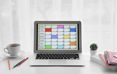 Photo of Modern laptop with calendar on screen in office