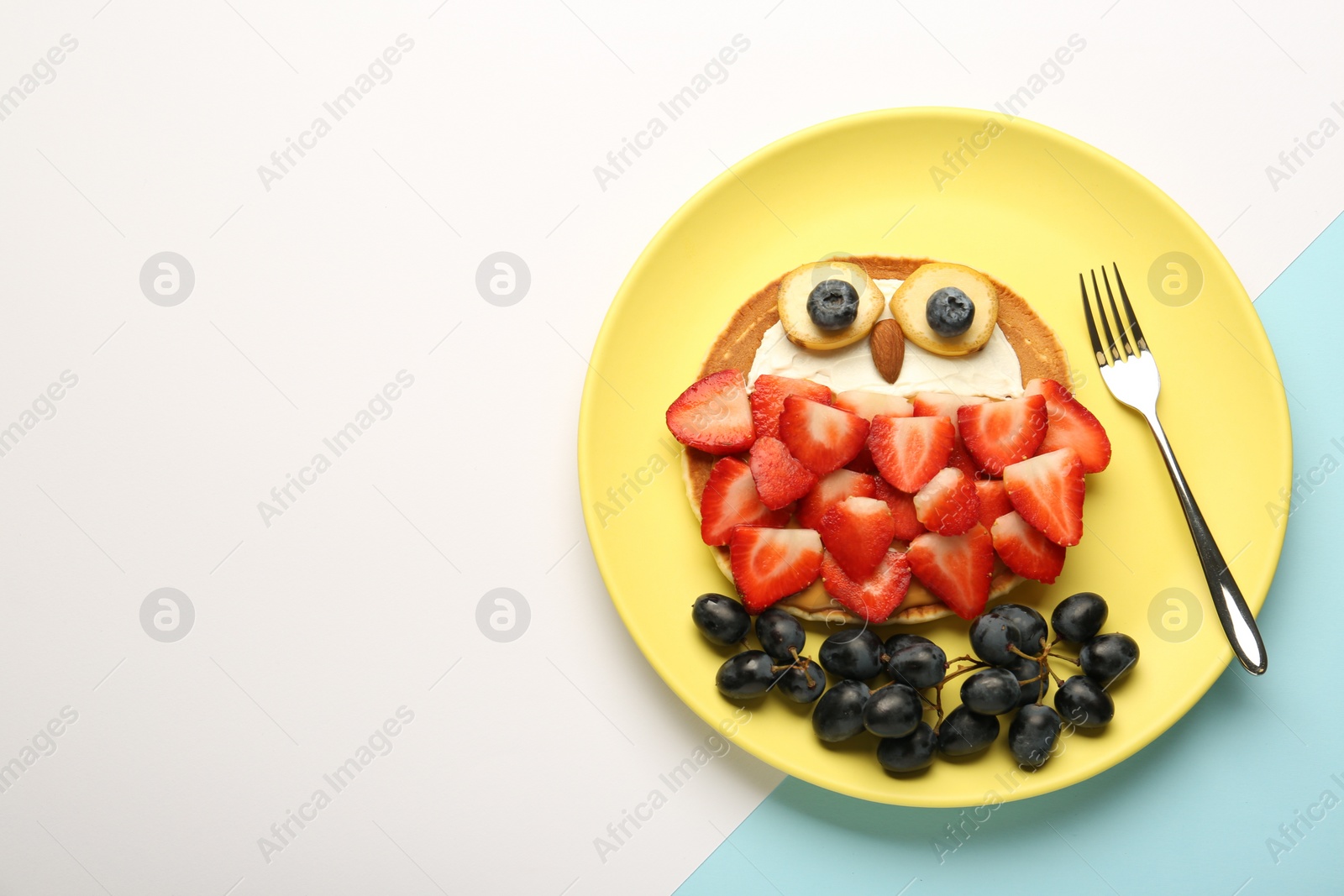 Photo of Creative serving for kids. Plate with cute owl made of pancakes, berries, cream, banana and almond on color background, top view. Space for text