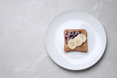 Photo of Toast with tasty nut butter, jam and banana on light table, top view. Space for text