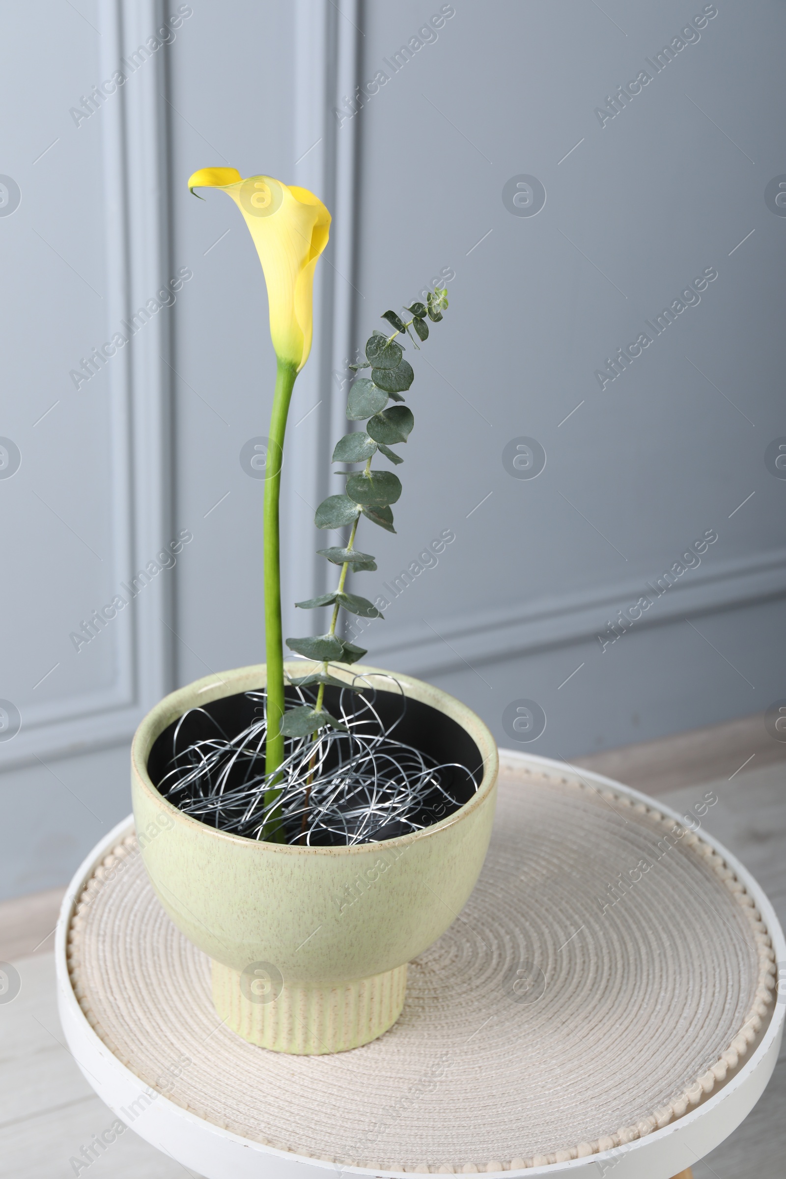 Photo of Stylish ikebana as house decor. Beautiful fresh calla flower and eucalyptus branch on table near white wall, space for text