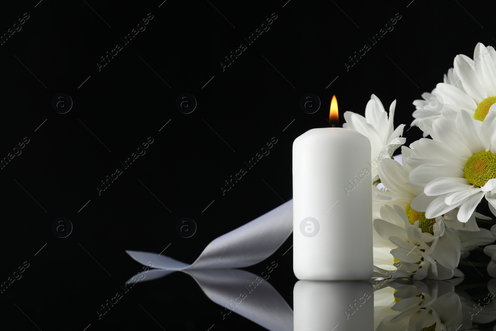 Photo of White chrysanthemum flowers and burning candle on black mirror surface in darkness, space for text. Funeral symbols