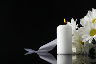 Photo of White chrysanthemum flowers and burning candle on black mirror surface in darkness, space for text. Funeral symbols