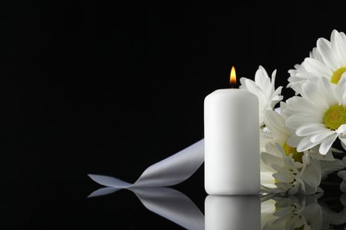 White chrysanthemum flowers and burning candle on black mirror surface in darkness, space for text. Funeral symbols