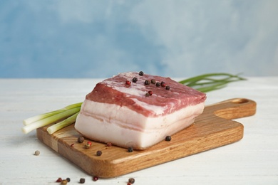 Board with pork fatback, peppercorn and onions on white wooden table