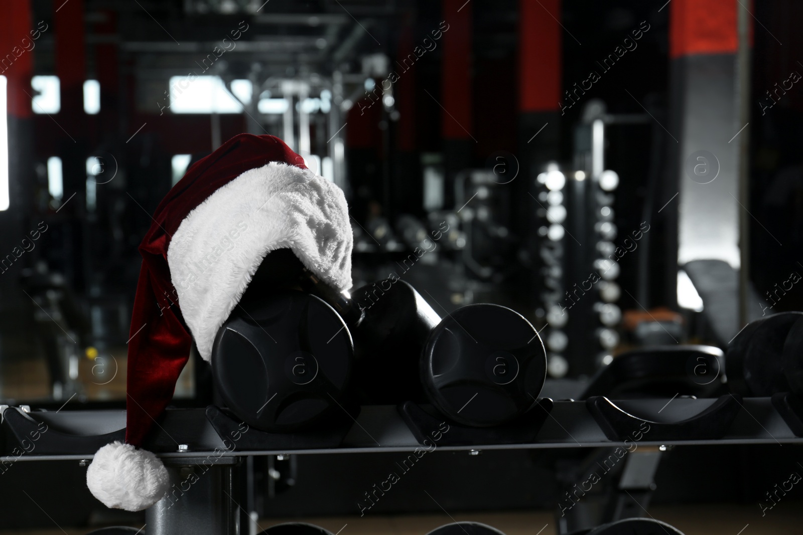 Photo of Santa hat on stand with dumbbells in modern gym