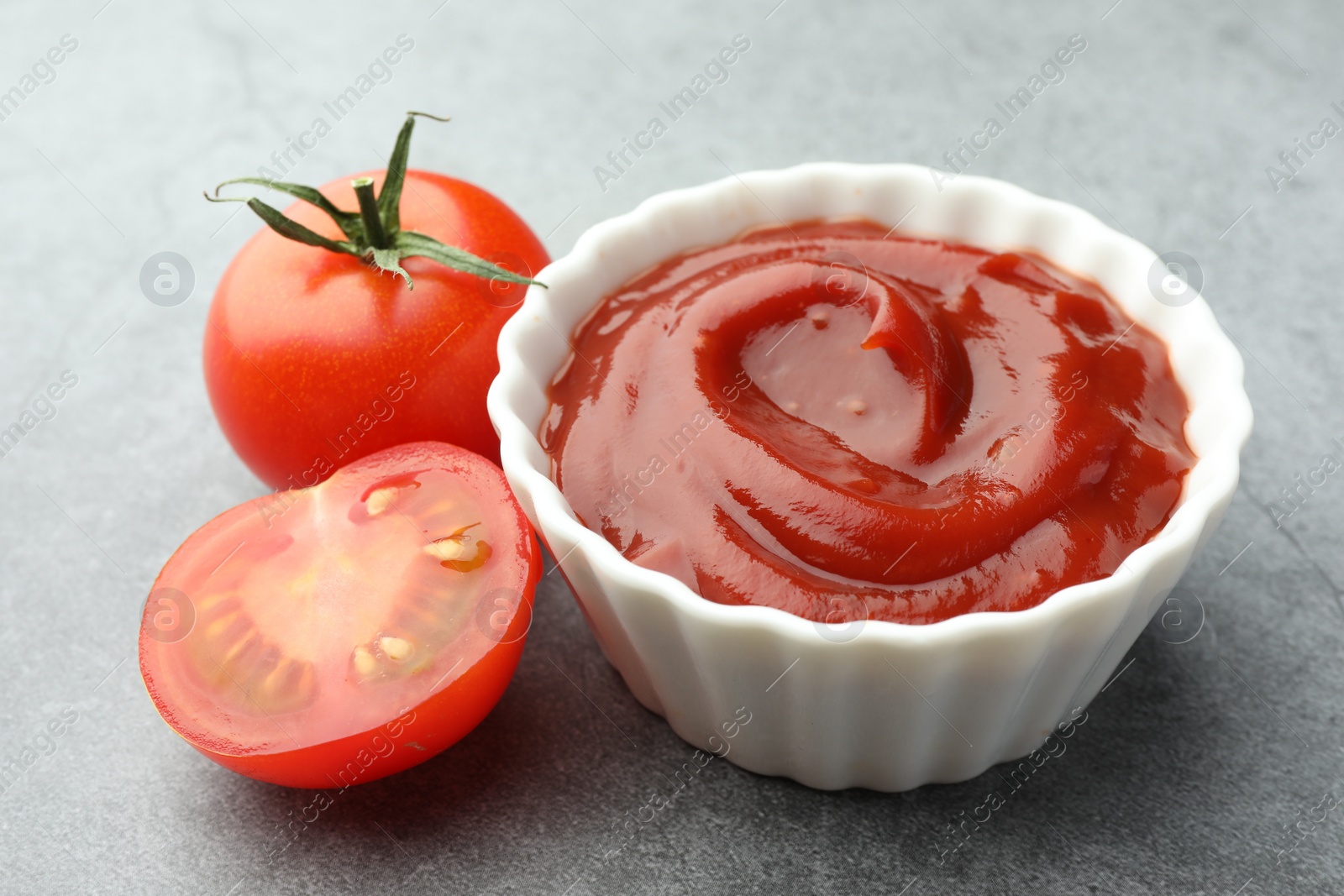 Photo of Bowl of tasty ketchup and tomatoes on light grey table, closeup