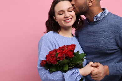 Photo of Happy couple celebrating Valentine's day. Beloved woman with bouquetred roses on pink background, space for text