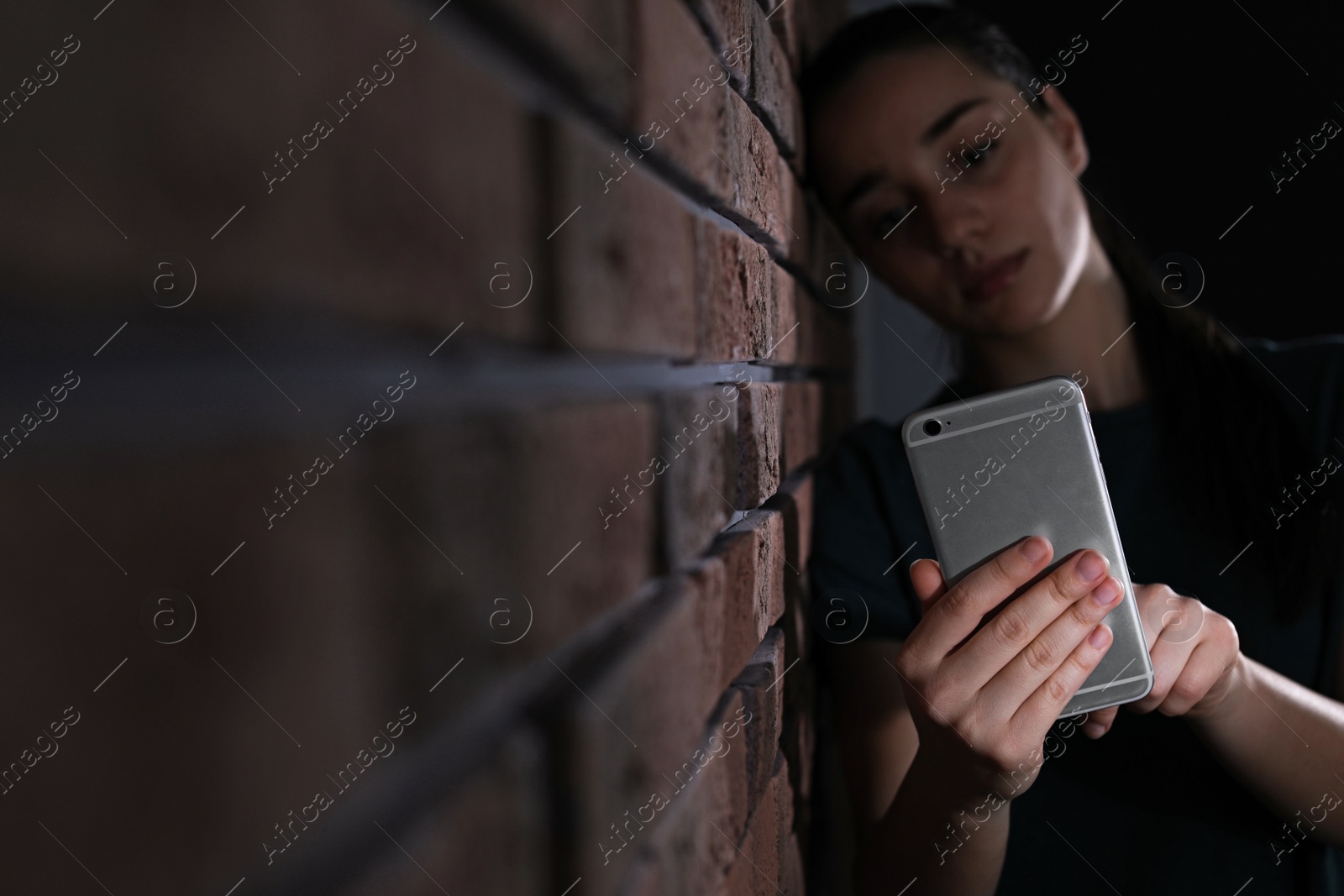 Photo of Sad woman with mobile phone near brick wall, space for text. Loneliness concept