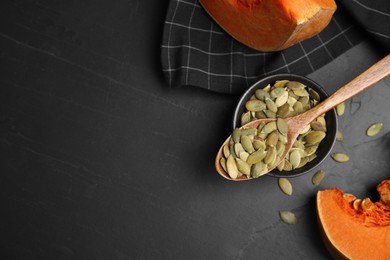 Bowl with seeds, wooden spoon and cut pumpkin on black table, flat lay. Space for text