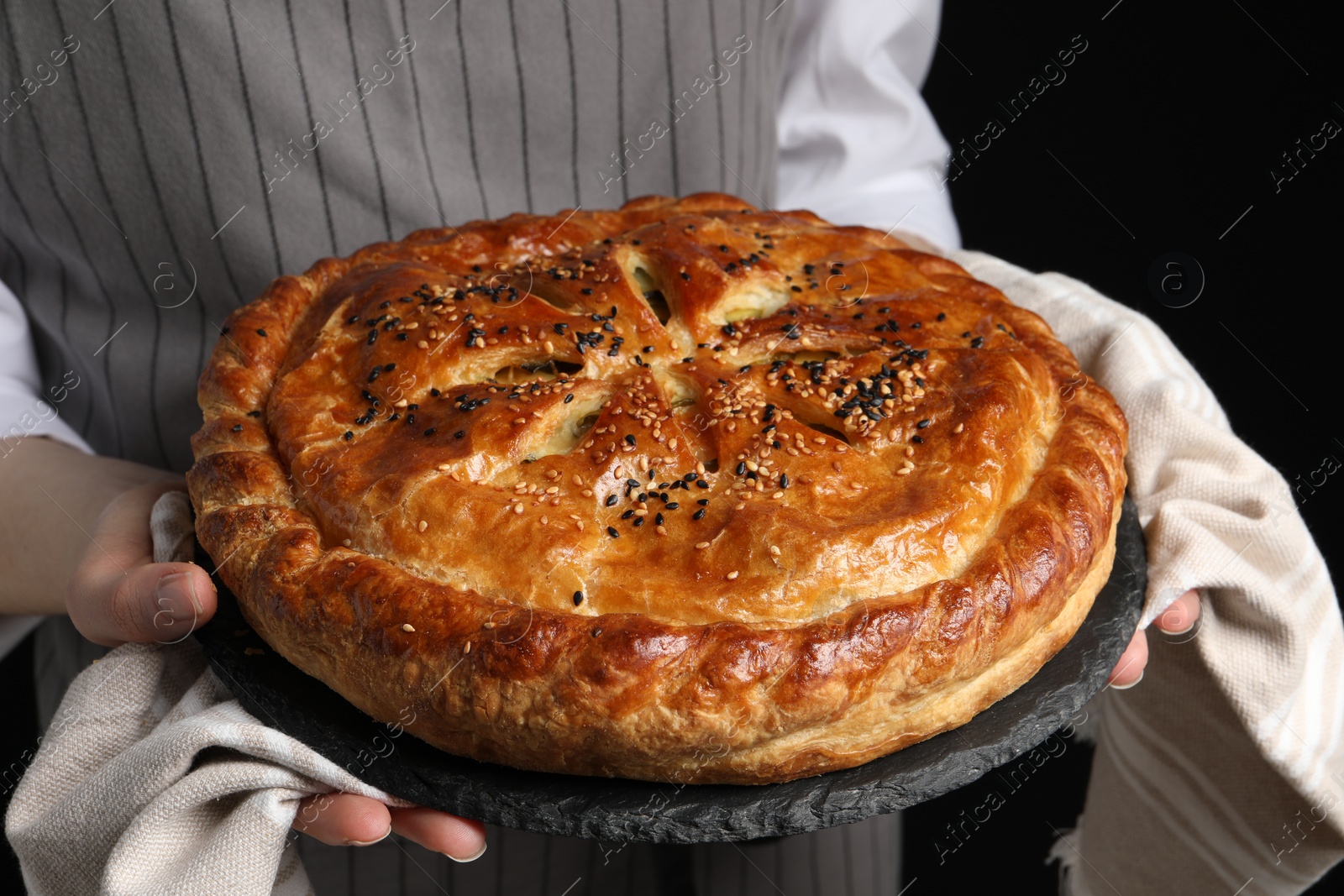 Photo of Woman holding tasty homemade pie on black background, closeup