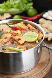 Saucepan with delicious Tom Yum soup and ingredients on table