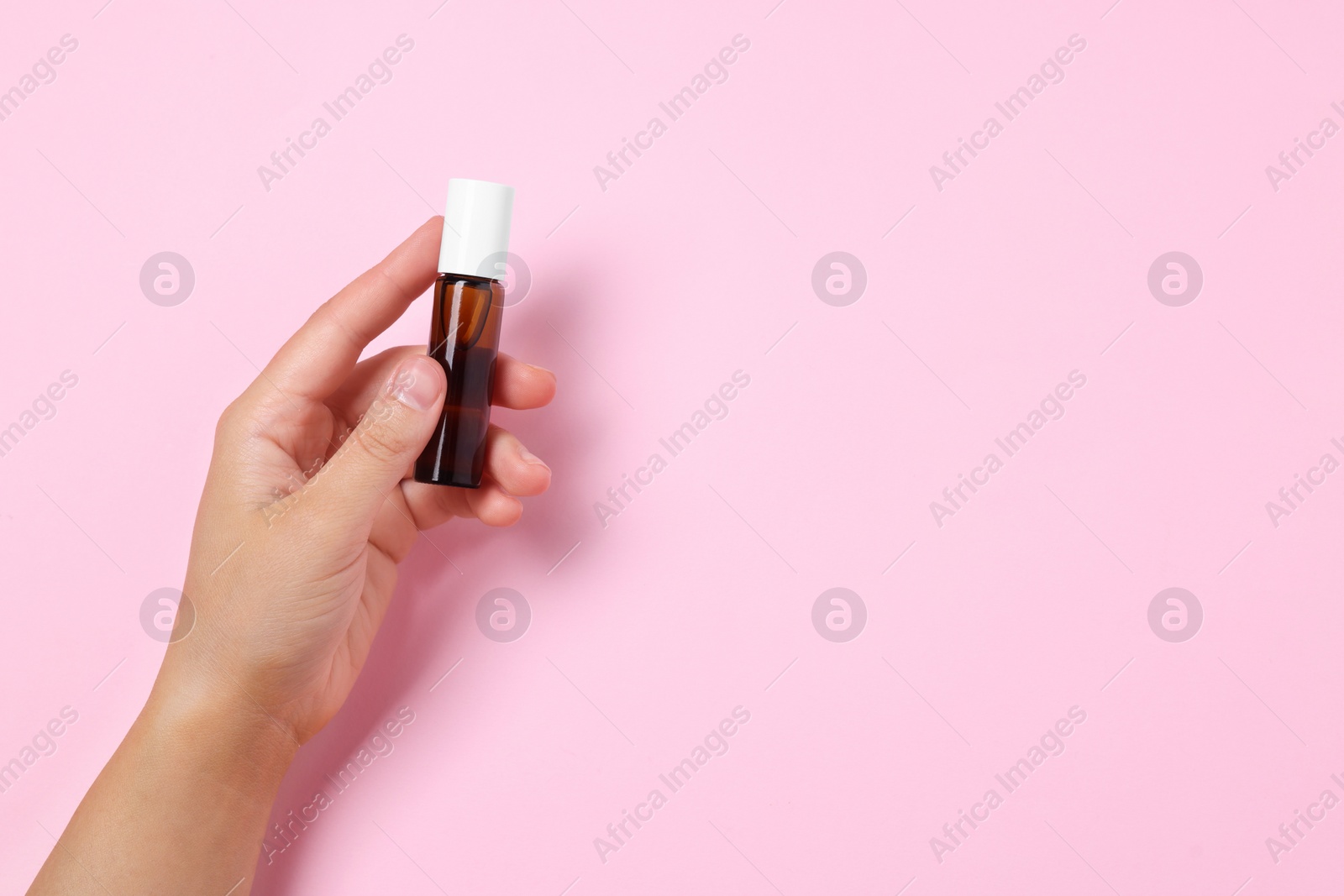 Photo of Woman with bottle of essential oil on pink background, closeup. Space for text