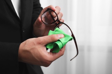 Photo of Man wiping glasses with microfiber cloth indoors, closeup. Space for text