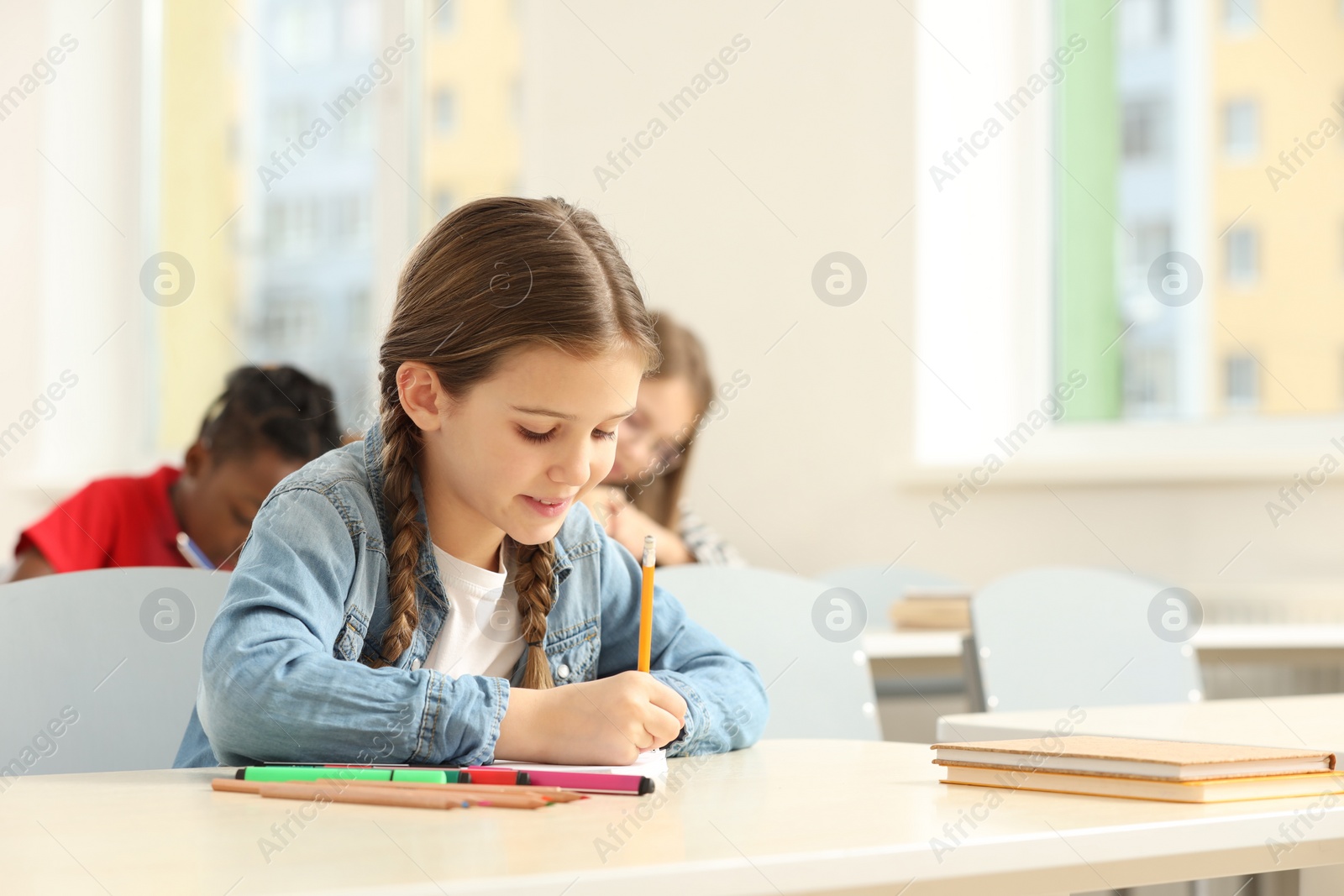 Photo of Cute little girl studying in classroom at school. Space for text