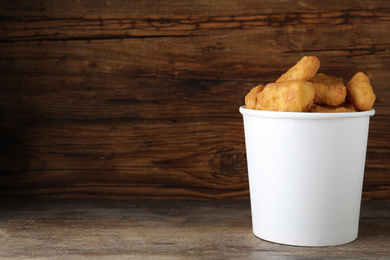 Photo of Bucket with tasty chicken nuggets on wooden table. Space for text