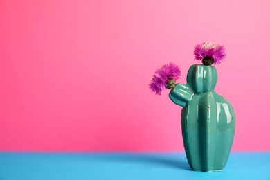 Photo of Trendy cactus shaped ceramic vase with flowers on table against color background