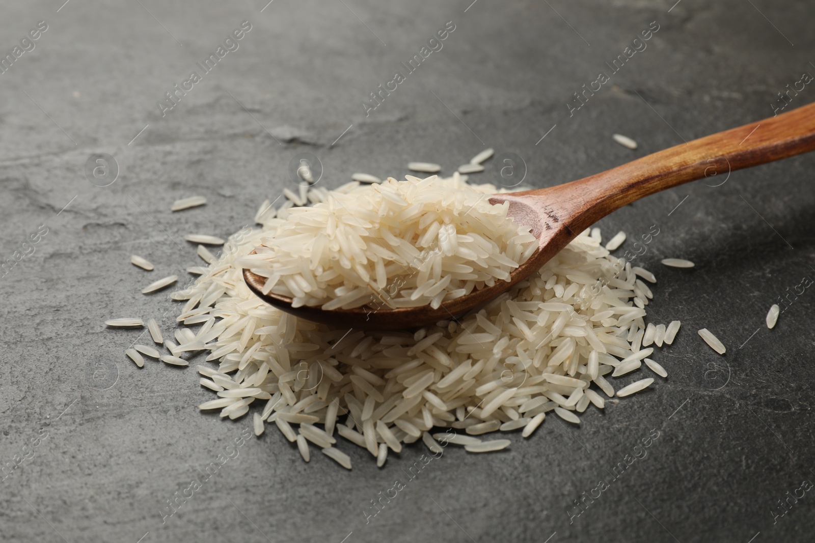 Photo of Raw basmati rice and wooden spoon on black table