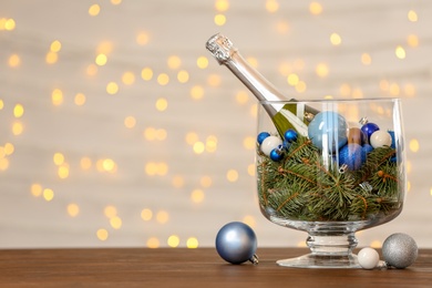 Photo of Bottle of champagne, fir tree branches and decor in glass vase on table. Christmas composition with space for text against blurred lights