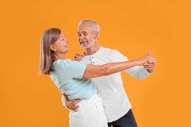 Photo of Senior couple dancing together on orange background