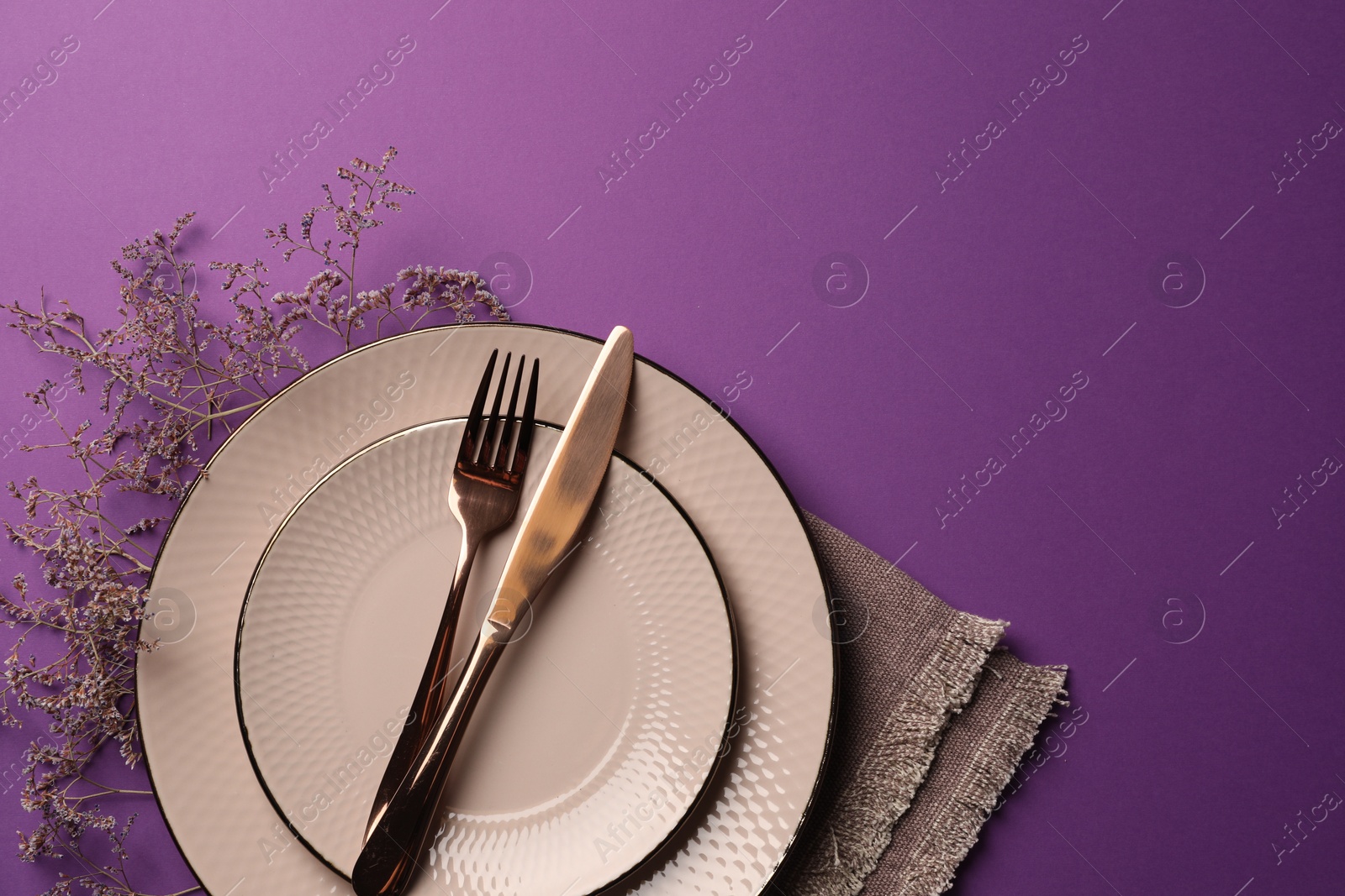 Photo of Stylish table setting. Plates, cutlery, napkin and floral decor on purple background, top view with space for text