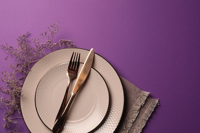 Photo of Stylish table setting. Plates, cutlery, napkin and floral decor on purple background, top view with space for text