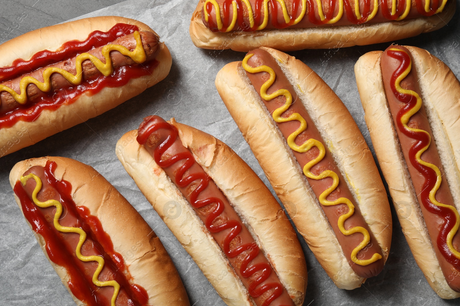 Photo of Fresh delicious hot dogs with sauces on parchment paper, flat lay