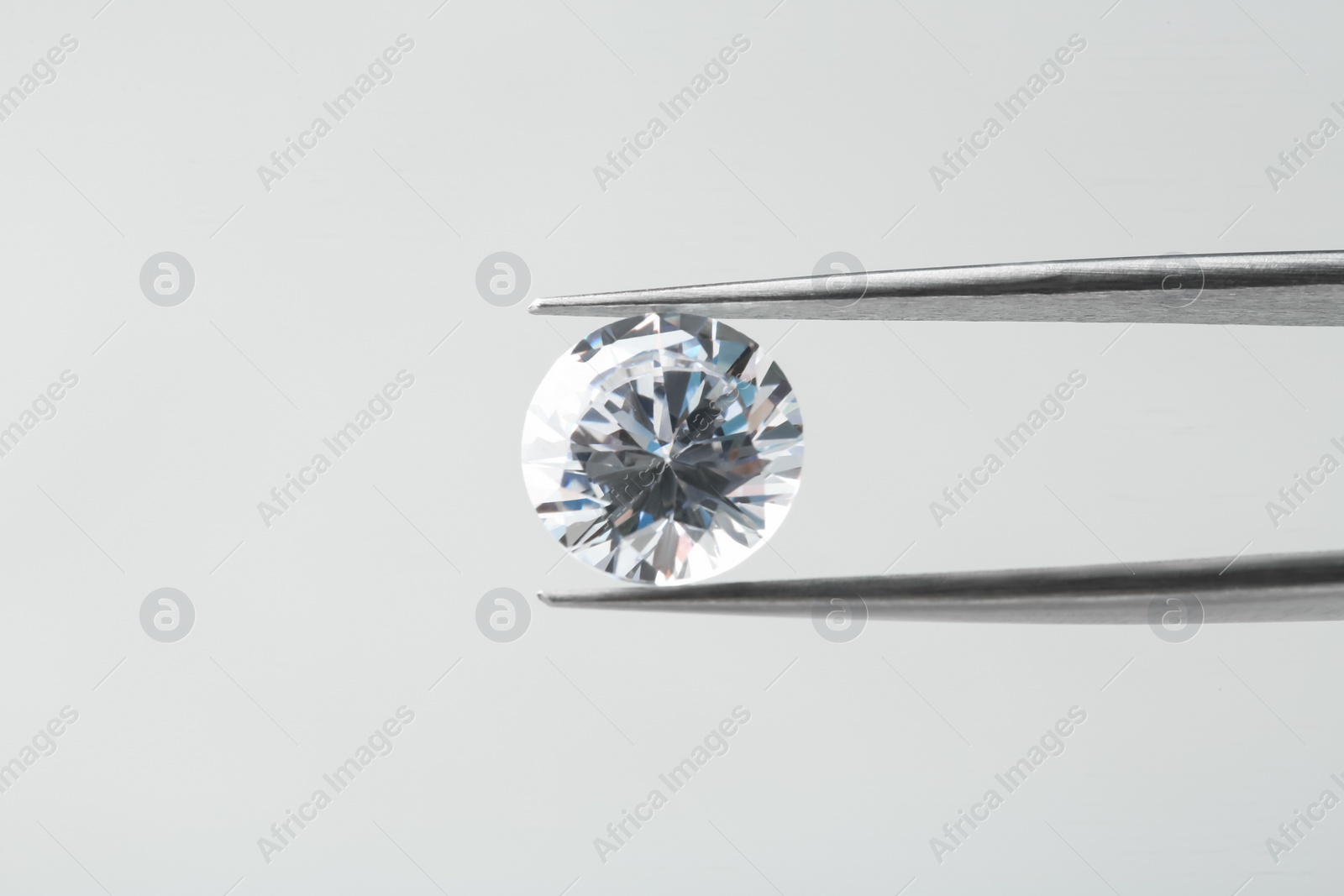 Photo of Tweezers with beautiful shiny diamond on light gray background, closeup. Space for text