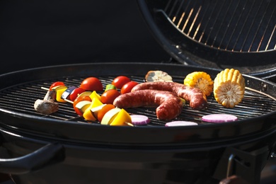 Photo of Tasty sausages and vegetables on modern barbecue grill