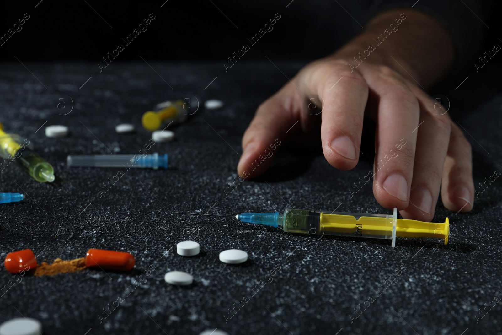 Photo of Addicted man and different hard drugs on black textured table, closeup