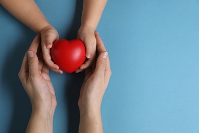 Mother and her child holding red decorative heart on light blue background, top view. Space for text