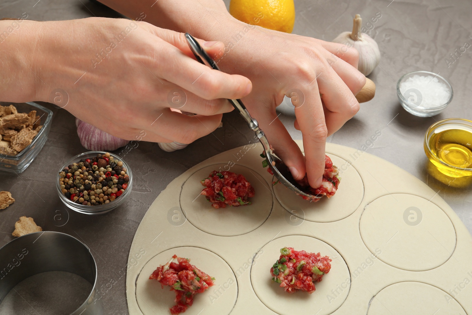 Photo of Woman cooking delicious gyoza at light grey table, closeup