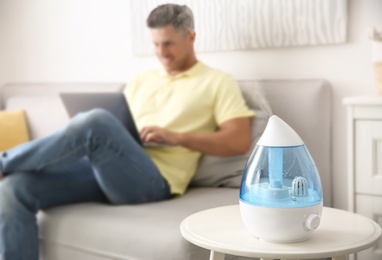 Photo of Modern air humidifier and blurred man on background