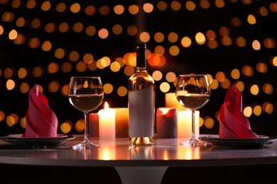 Photo of Romantic table setting with bottle of wine and burning candles against blurred background