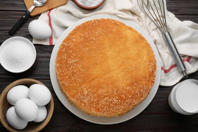 Plate with delicious sponge cake and ingredients on dark wooden table, flat lay