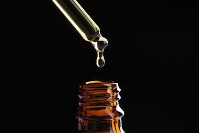 Photo of Dripping tincture from pipette into bottle on black background, closeup