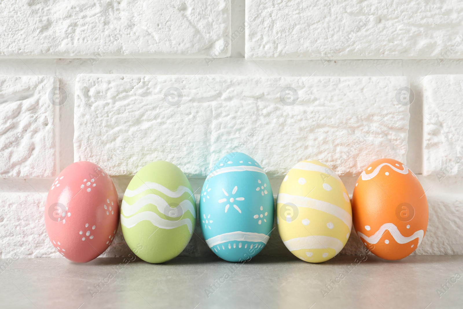 Photo of Colorful painted Easter eggs on table near brick wall, space for text