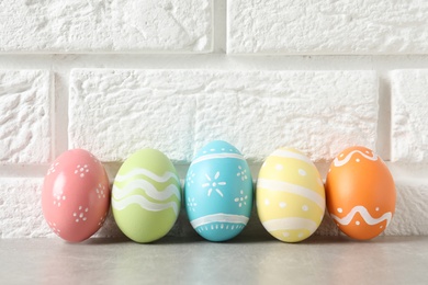 Colorful painted Easter eggs on table near brick wall, space for text