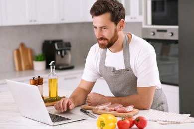 Man making dinner while watching online cooking course via laptop in kitchen