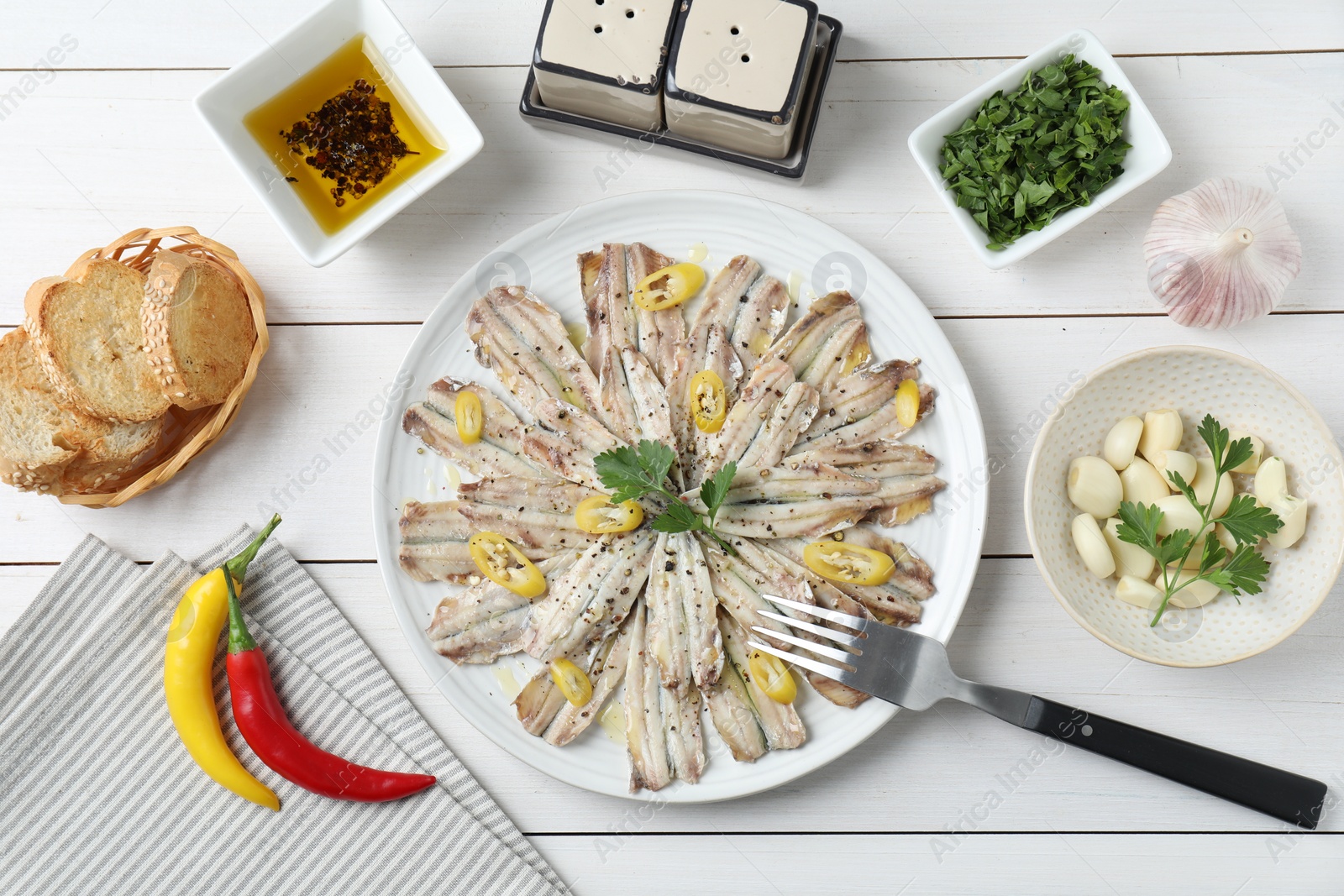 Photo of Tasty pickled anchovies served on white wooden table, flat lay