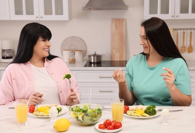 Photo of Happy overweight women having healthy meal together at table in kitchen