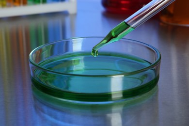 Dripping green liquid into Petri dish with sample on table, closeup