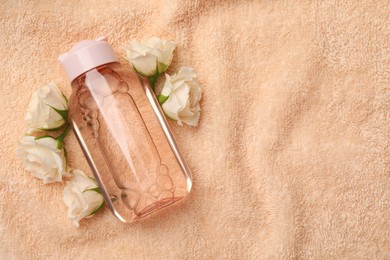 Photo of Bottle of micellar cleansing water and flowers on pink towel, flat lay. Space for text