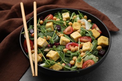 Photo of Bowl of tasty salad with tofu, chickpeas and vegetables on brown textured table, closeup