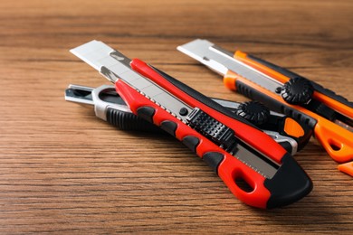 Photo of Different utility knives on wooden table, closeup. Construction tool