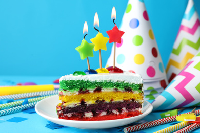 Photo of Piece of cake with candles and birthday decor on light blue background